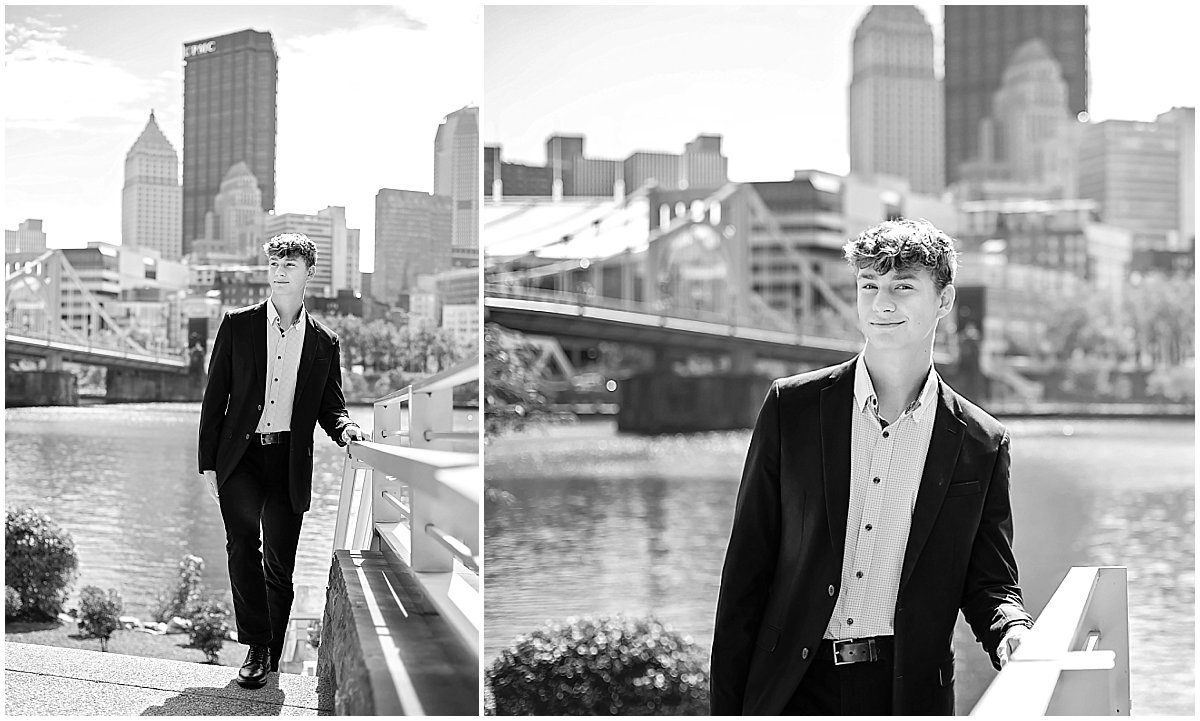 black and white images of a senior guy in a dark suit standing along the North Shore with the Pittsburgh skyline behind him.