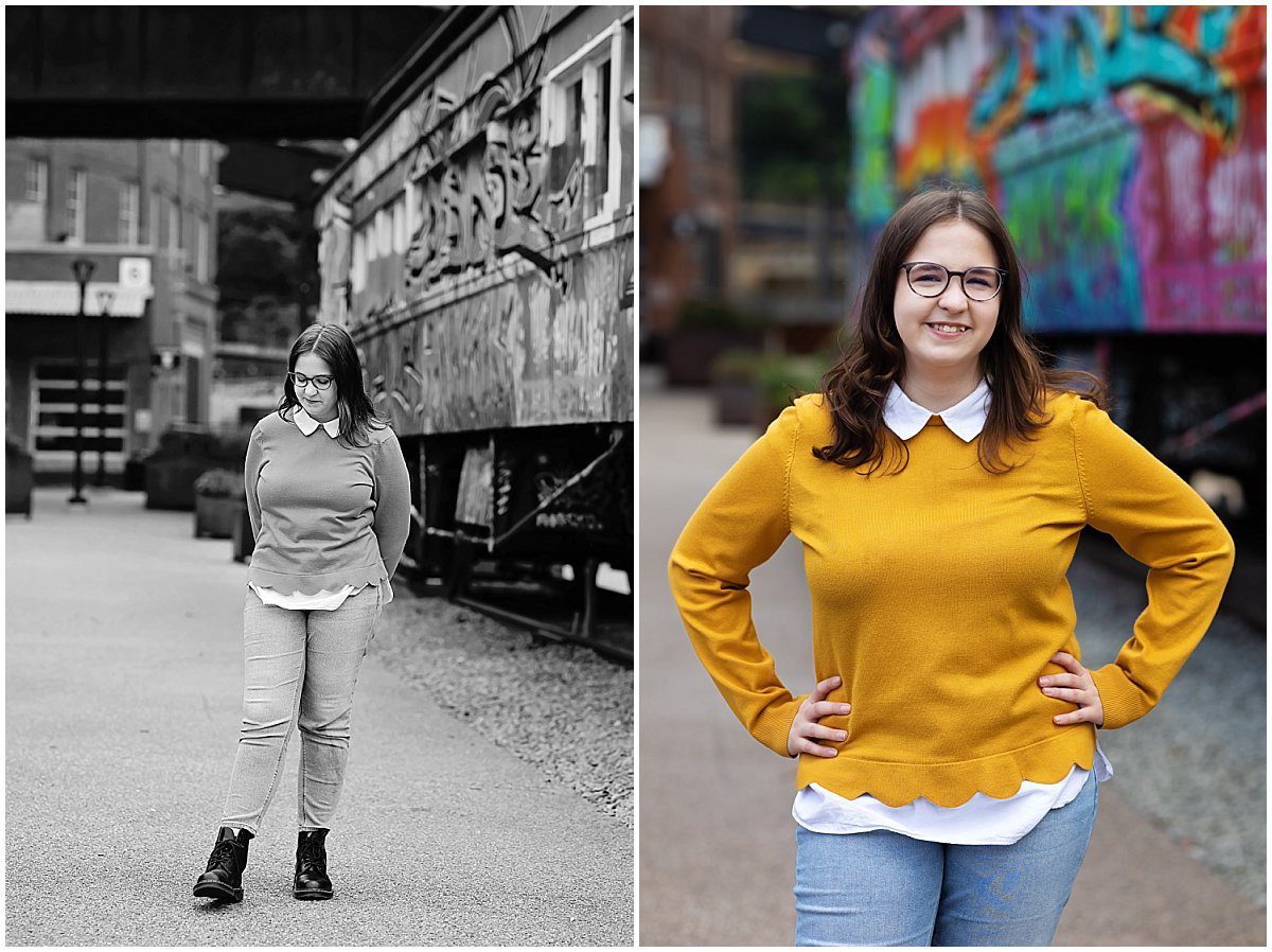 images of a senior girl standing next to a train caboose covered in graffiti at Pittsburgh's Highline. She has long dark hair, black framed glasses and a yellow sweater with jeans.