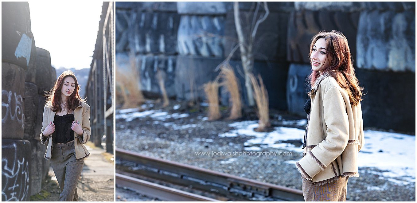 images of a senior girl walking around an industrial alley in Pittsburgh's Strip District. She's wearing beige plaid pants and a beige jacket with fur accents. There are large industrial tires and tall grasses in the background as well as a dusting of snow.