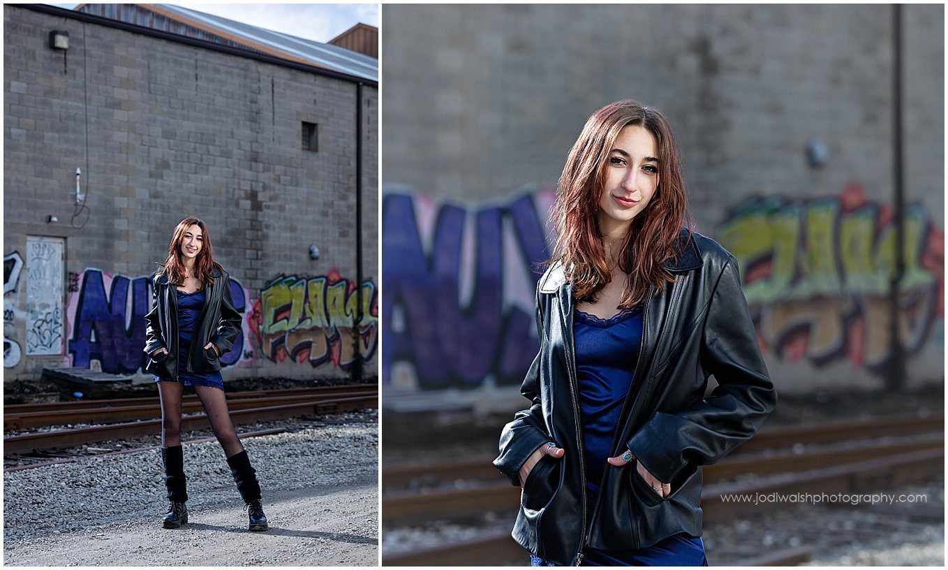 images of a senior girl in an alley near Pittsburgh's Strip District. She's wearing a black leather jacket over a blue silk dress and boots with black legwarmers. There is graffiti on the warehouse walls behind her.