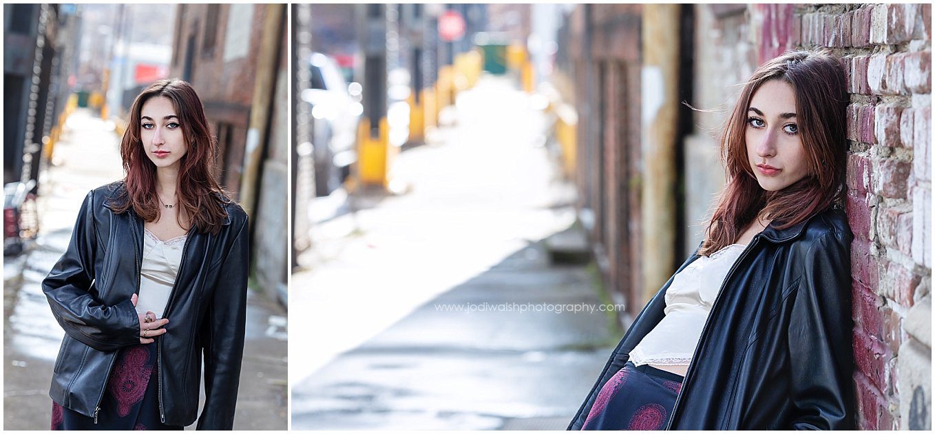 images of a senior girl along the sidewalk in the Strip District of Pittsburgh. She's wearing a black leather jacket over a white top with a black and red skirt.