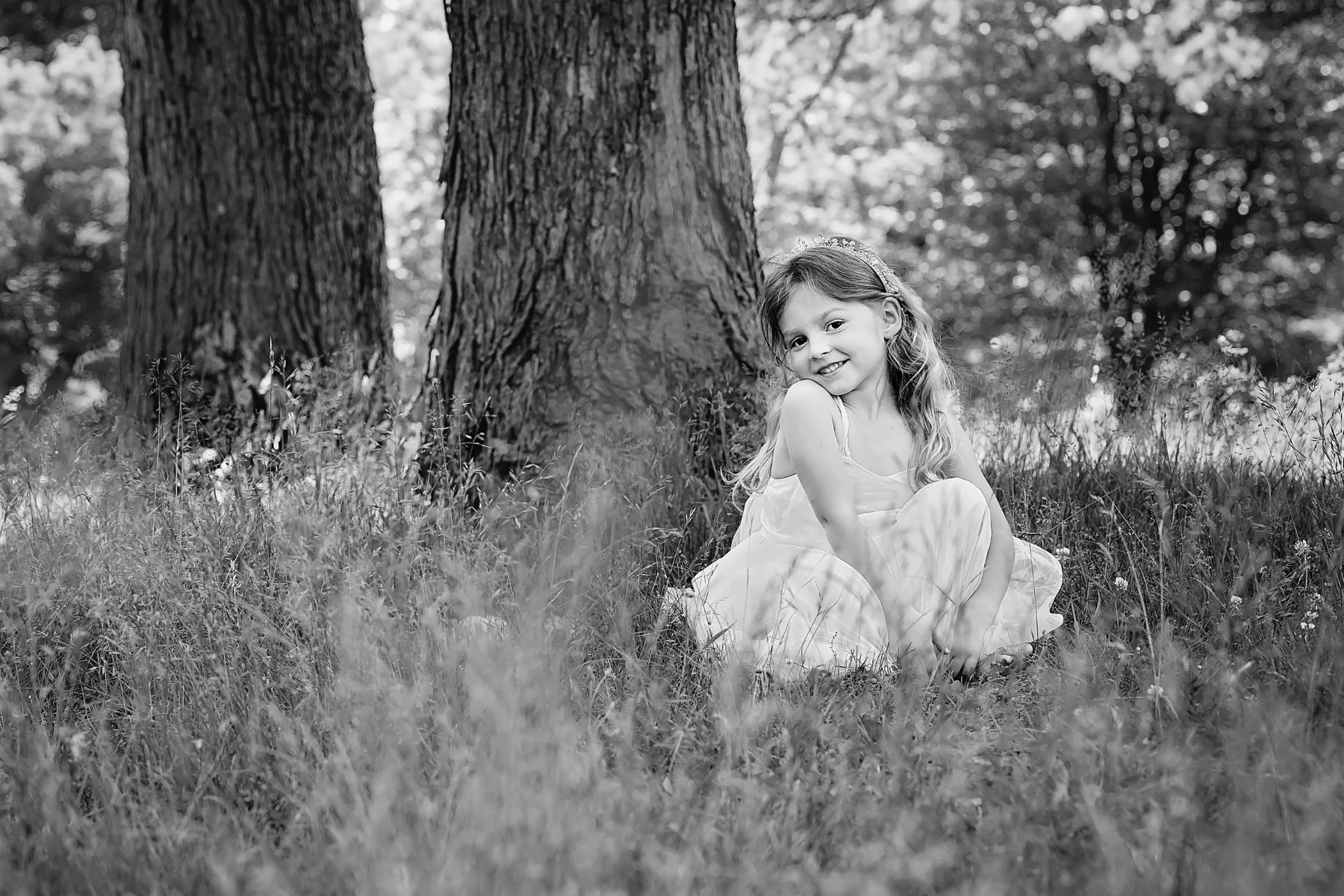 black and white image of a little girl sitting the tall grass next to a tall tree in North Park near Pittsburgh.