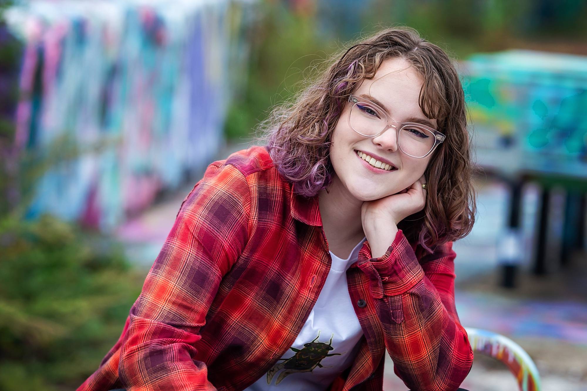 image of a senior girl sitting on a bench at the Color Park near Pittsburgh's Southside neighborhood. She's wearing a red plaid shirt and has brown, wavy hair with violet tips.