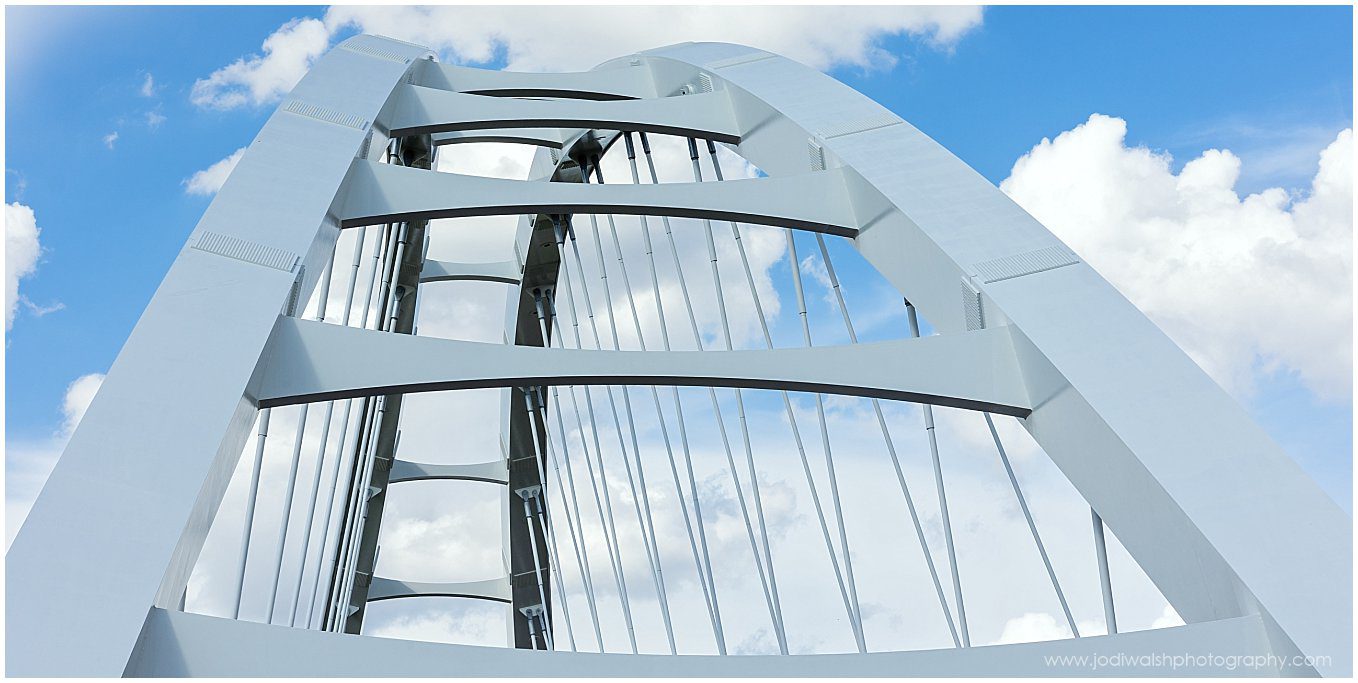 image of the top of the Walterdale Bridge in Edmonton, Alberta.  There are white arches with the blue sky in the background.