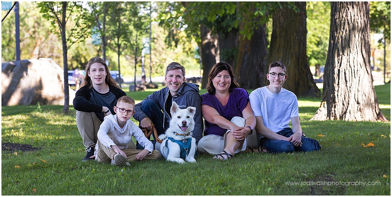 image of a family sitting in the grass together with their white dog.