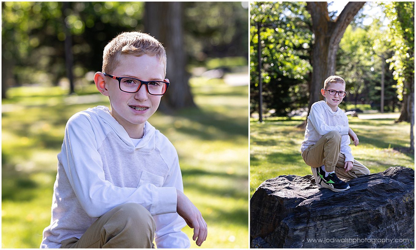 image of a little boy sitting on a large rock at a park. He's wearing a white sweater and glasses.