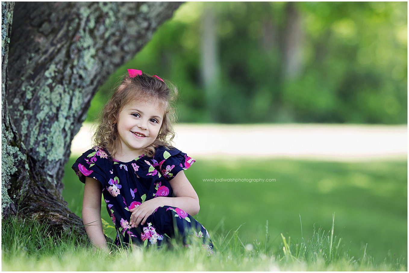 image of a little girl wearing a navy dress with flowers. She's sitting under a shade tree in Moraine State Park near Pittsburgh.