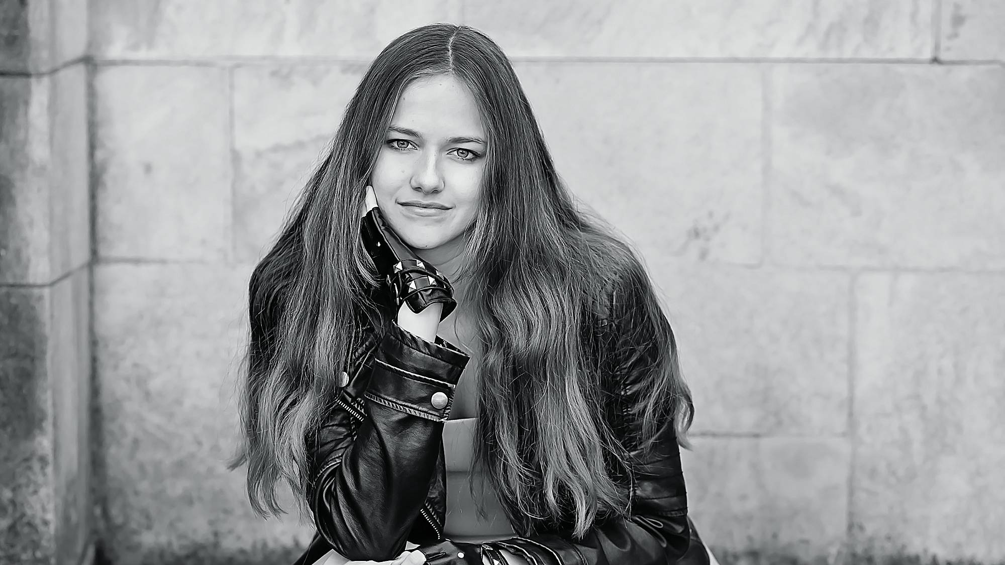black and white image of a senior girl wearing a black leather jacket and black leather fingerless gloves. She has long wavy hair and is smirking at the camera