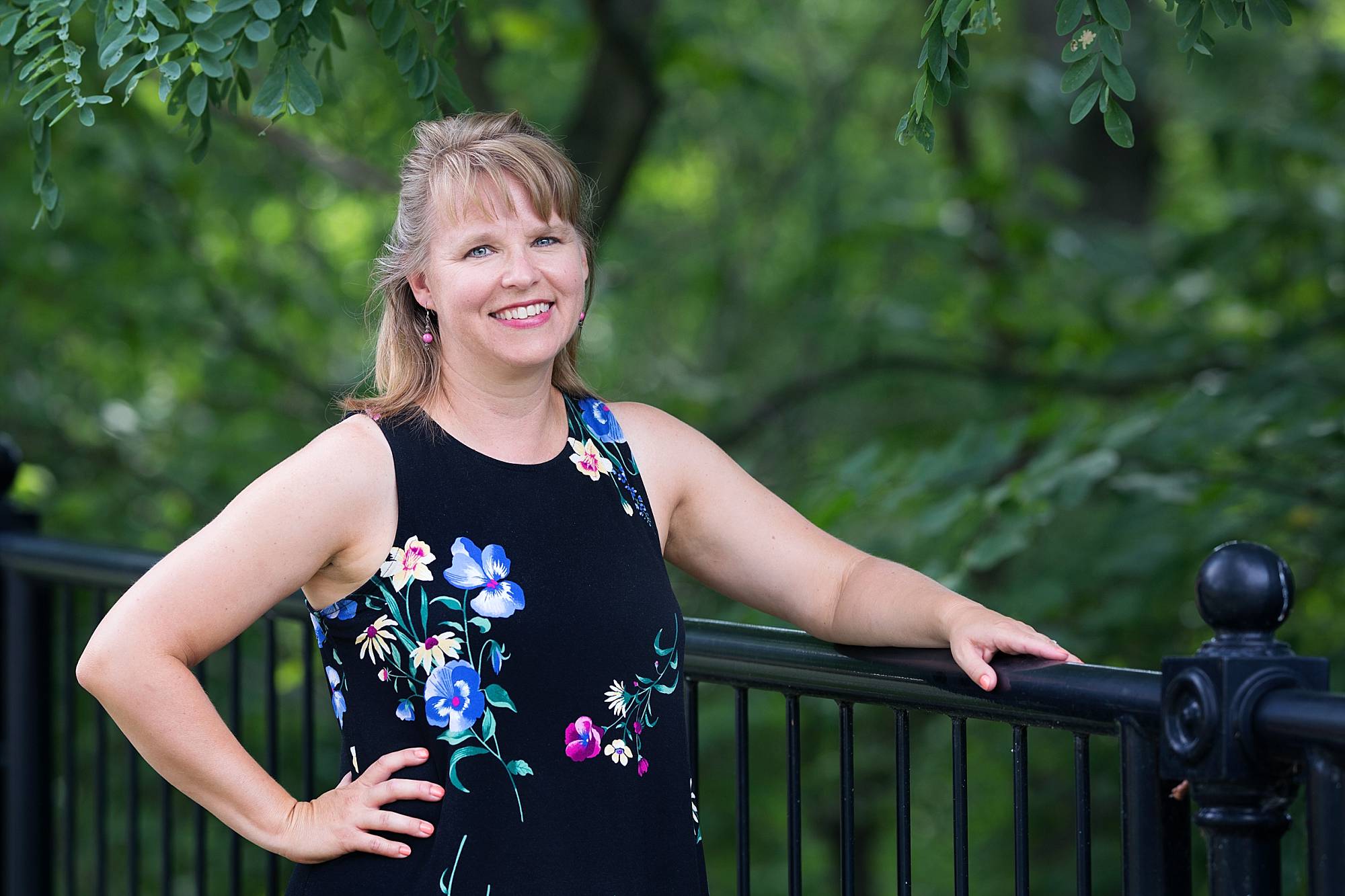 image of Theresa Grosh, designer and owner of Naptime Inspirations where she creates handmade accessories. She's a blonde woman wearing a navy sleeveless, flowered dress.