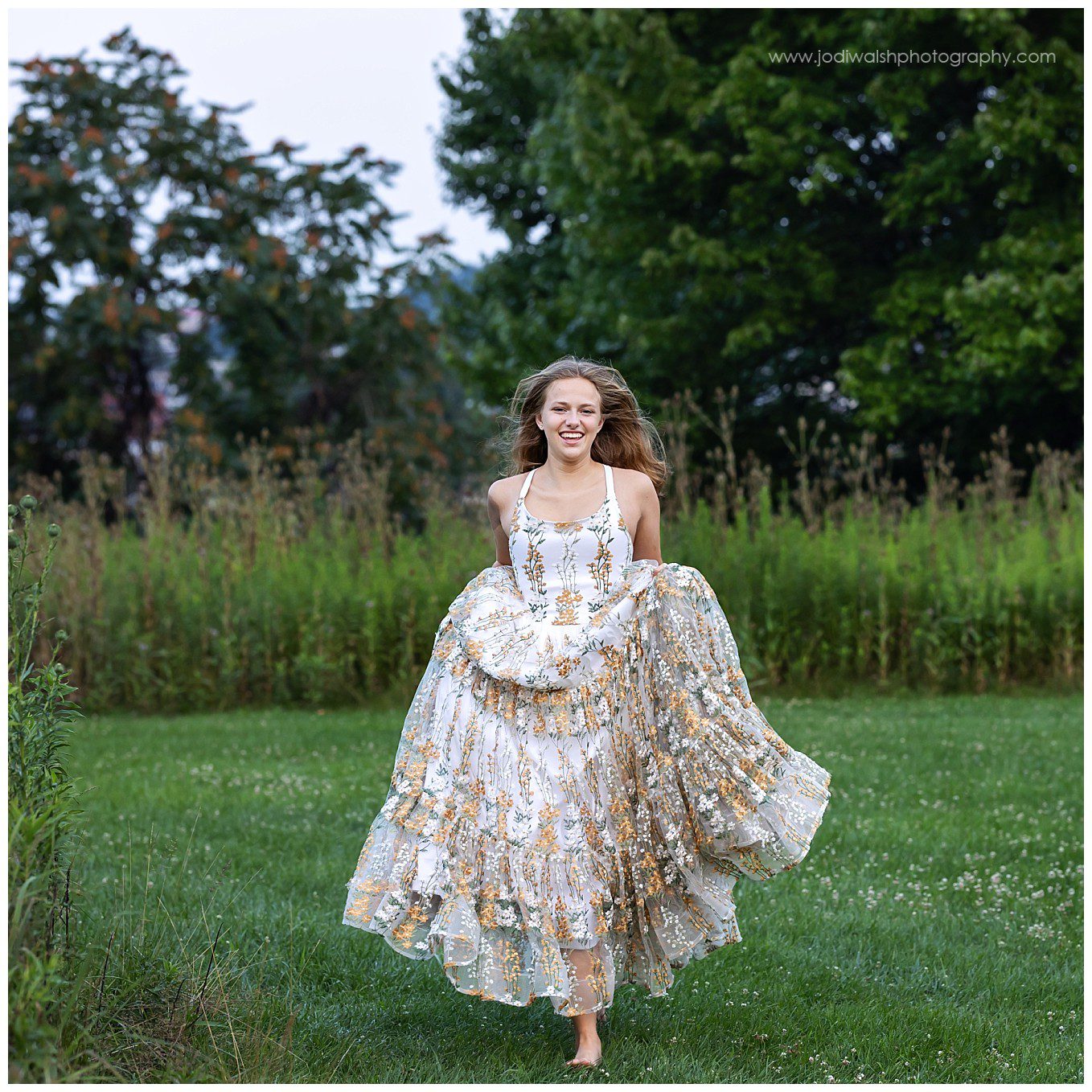 image of a senior girl running in a field and wearing a couture gown. She has long blond hair that is down and flowing behind her.