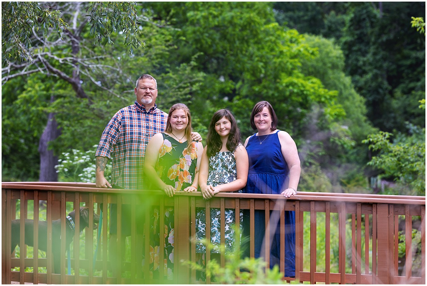 image of a family with mom, dad, and teen daughters standing on a wooden bridge over a creek in North Park, Pittsburgh
