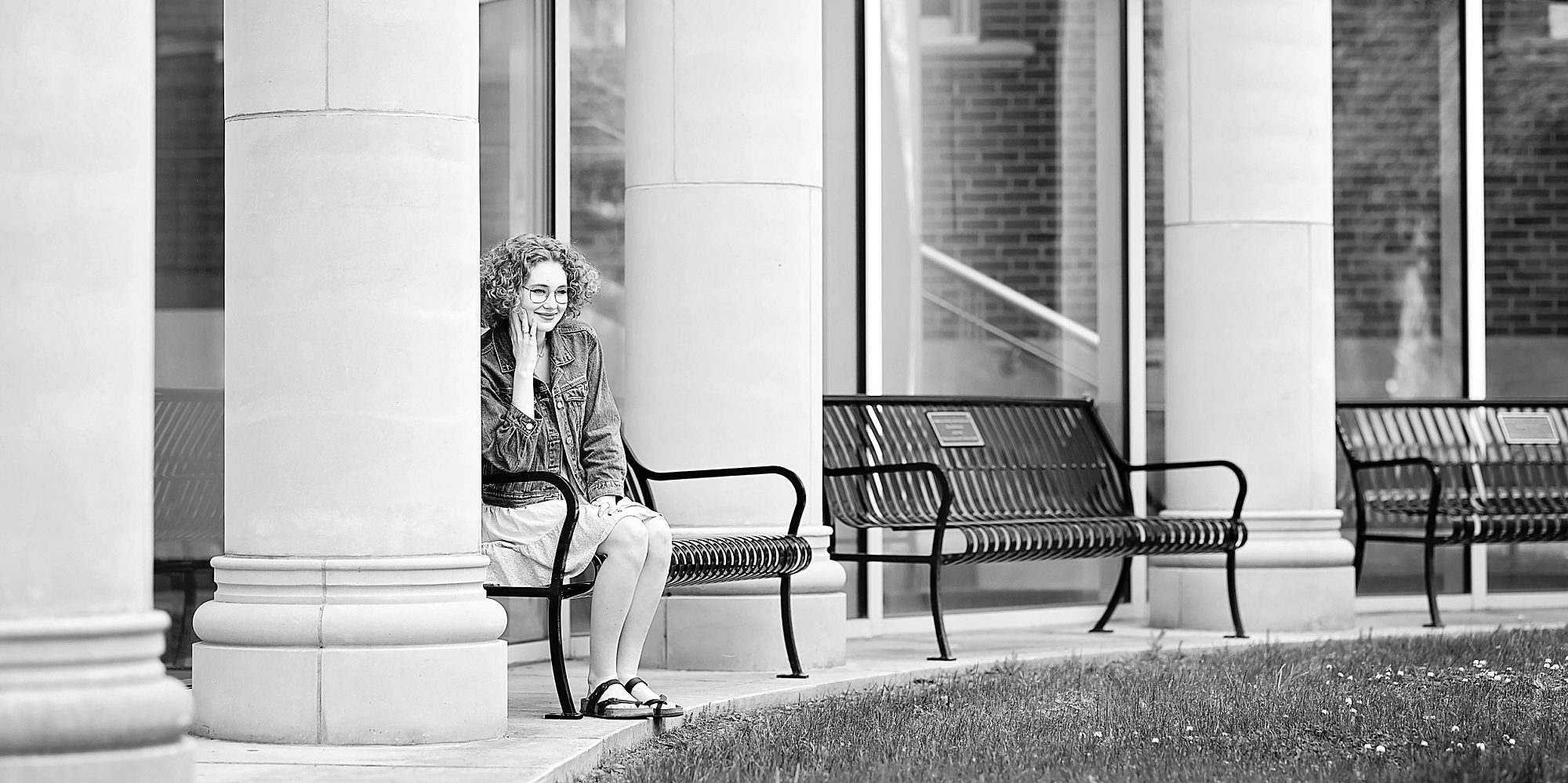 Black and white photo of a senior girl sitting on a bench between white columns at Indiana University of Pennsylvania.