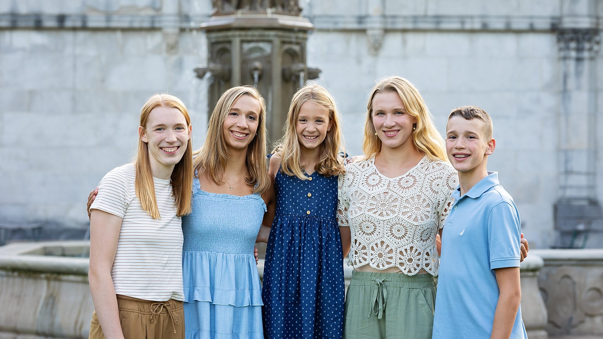 siblings, sisters and one brother standing arm in arm in front of a fountain at Mellon Park