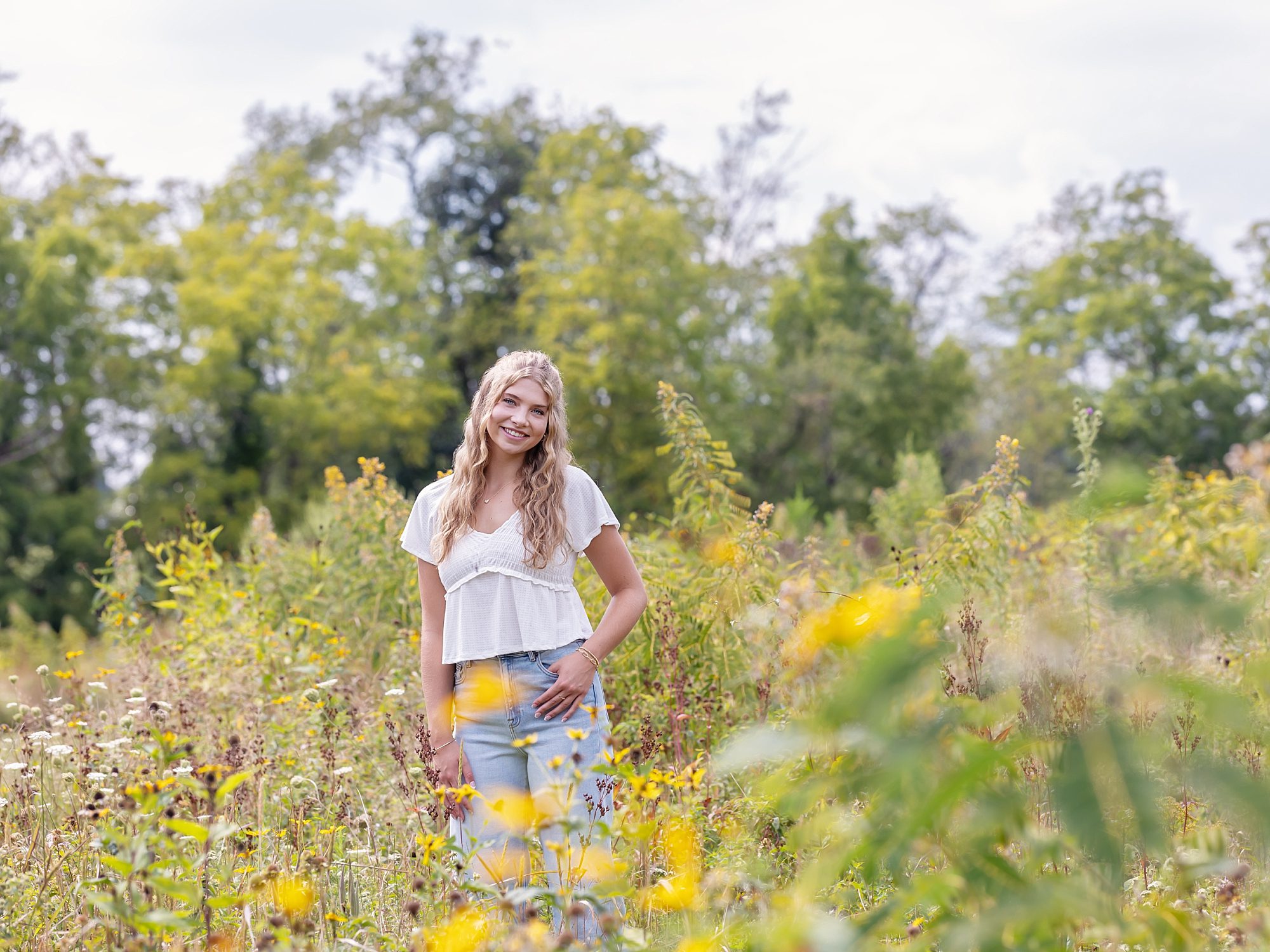 image of a blond teen girl wearing a white t-shirt and blue jeans standing in a field of summer wildflowers