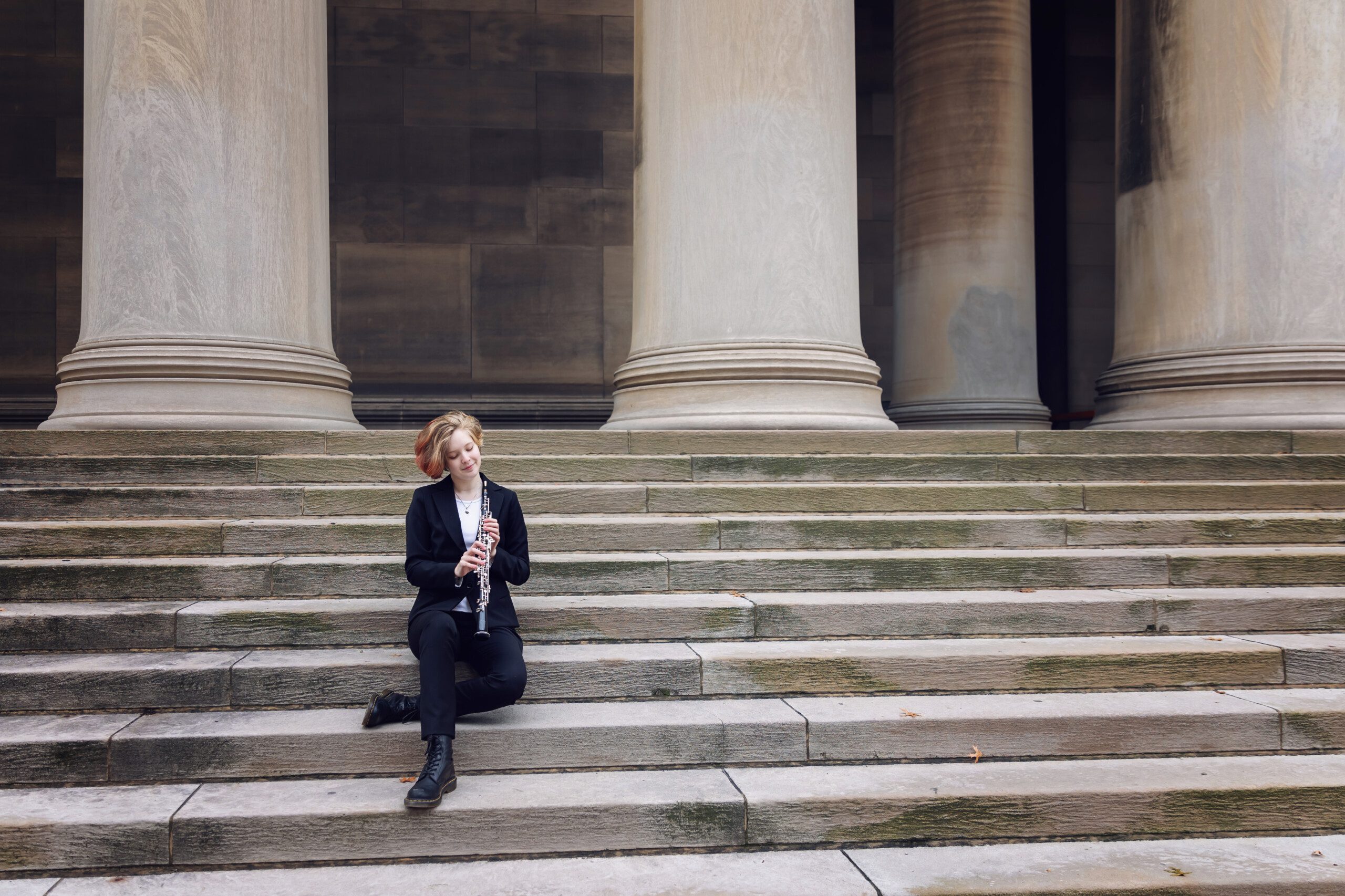 senior oboe player wearing a black suit, sitting on the steps at Mellon Institute in Pittsburgh